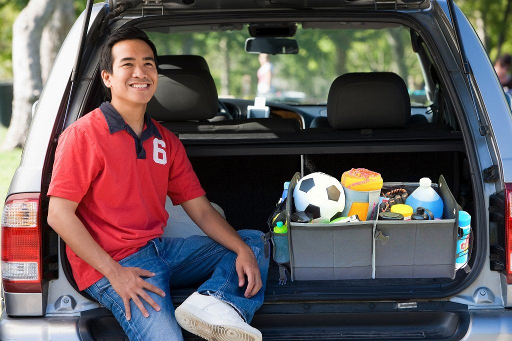 kid sitting in the back of an suv with his sports gear in the trunk organizer